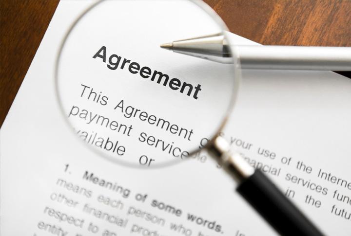 A contract with agreement written at the top and a magnifying glass over the top of the paper