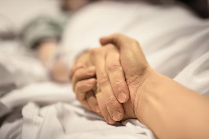 close up of holding hands with a person in a hospital bed