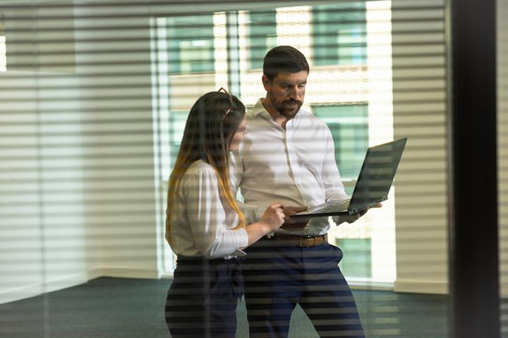 woman and man standing up looking at a laptop screen