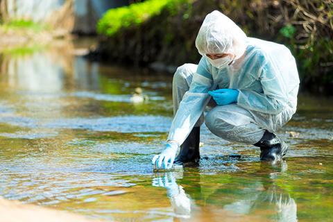 Person in ppe collecting sample from river