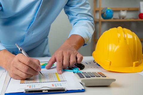 Close up of man's hands reviewing some documentation with a calculator and a hard hat beside him