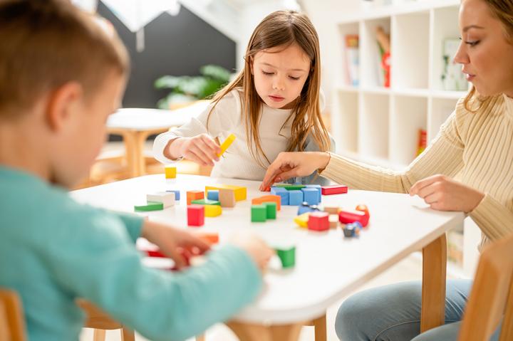 Two kids sitting at a table with an adult playing with colourful building blocks