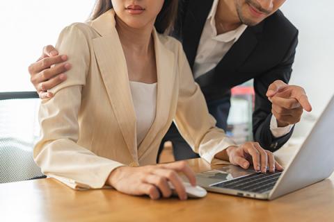 Man with arm around a female colleague, looking at a laptop