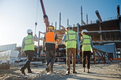 A group of people in high-vis jackets walking away from the camera and walking towards a building under construction