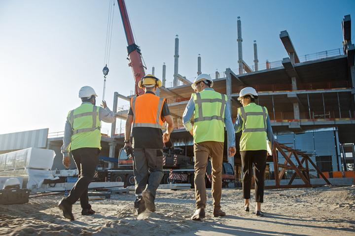 A group of people in high-vis jackets walking away from the camera and walking towards a building under construction