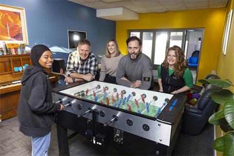 A group of people standing around a football table in a brightly coloured room