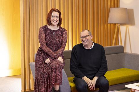 Paula Normington and Chris Maddock sitting on a green and grey sofa with a lamp in the background