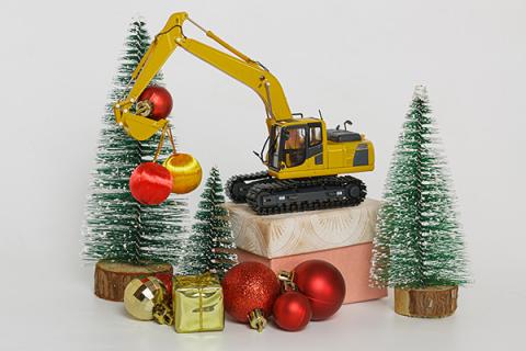 A toy excavator on wrapped presents with baubles and toy Christmas trees placed around