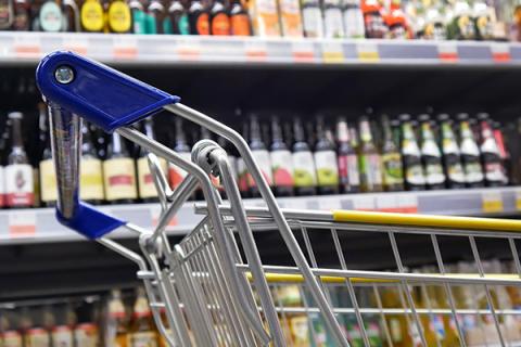 Shopping trolley next to supermarket shelves of alcohol