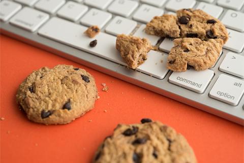 Three chocolate chip cookies lying on a laptop keyboard