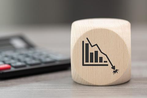 A wooden cube showing a downward-trending graph, with a calculator in the background