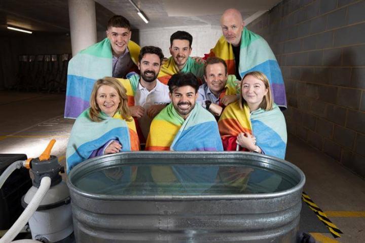 a group of people wearing colourful towels around their shoulders sitting in front of a metal bath filled with water