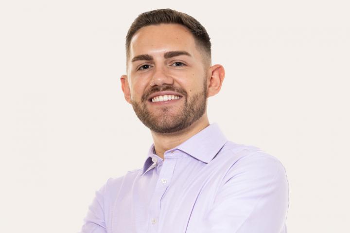 Jordon Goodman, wearing a white almost lilac shirt, smiling into the camera