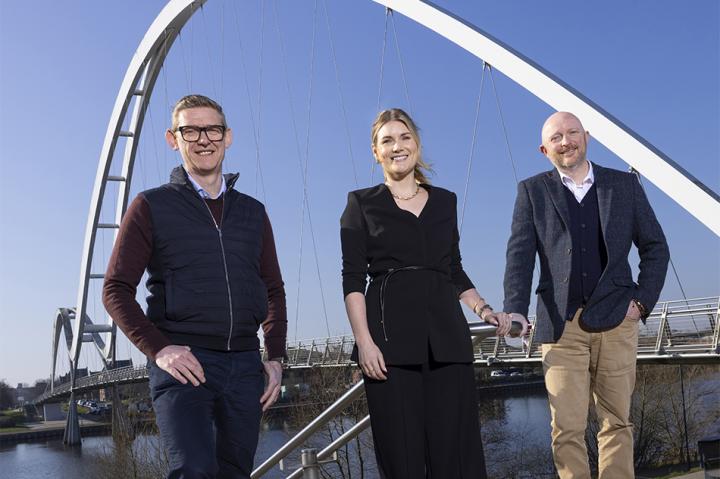 L-R Anthony Evans, Leah Duffield and David Towns standing in front of Teesside's Infinity Bridge against a blue sky