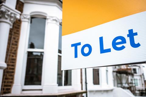 A yellow and white sign reading: to let, in blue writing, with a terraced property visible in the background